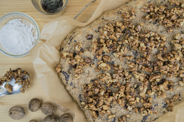 Homemade cake with roasted walnuts from above cropped shot of cake on baking paper with ingredients over wooden table surface background