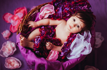 Funny girl looks up lying in basket full of cloth flowers