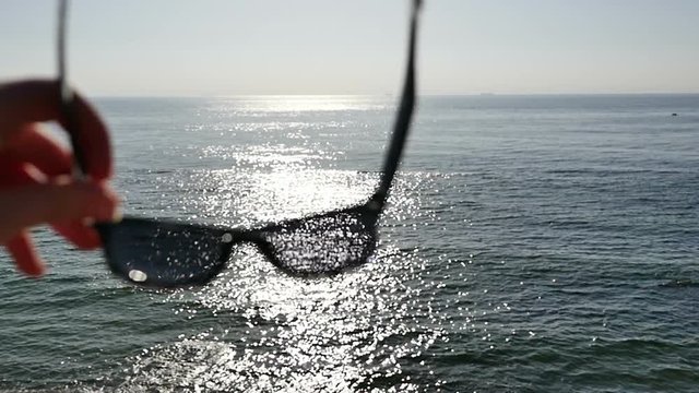 Look at the beautiful sea and sunset beach through sunglasses. Summer beach holidays and vacations. Sunglasses on the beach. View on the sea through dark sunglasses.Blue sunny sky. 