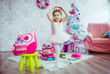 Obraz na płótnie Canvas Little girl poses like a ballerina standing on the carpet with toys