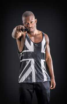 Young handsome black man holding a hand gun, on dark background in studio