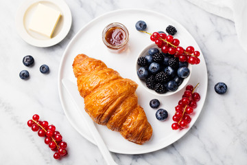 Croissant with fresh berries and butter on a marble texture background. Top view