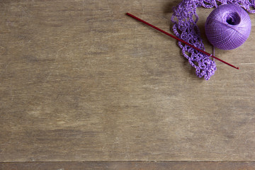 lilac clew of yarn with crochet hook on a wooden table