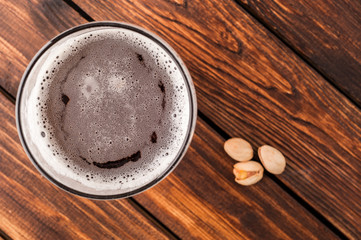 glass of dark cold frothy beer, nuts old wooden table