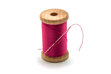 Isolated wooden spool of pink thread with a needle
