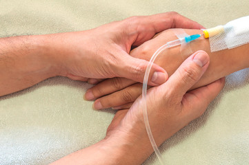 Man holding woman, patient, hand with a tube of medicine injection on a bed in a hospital
