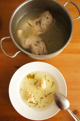 Chicken broth with chicken in metal pot and in white plate on wood background 