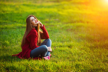 Happy young woman. Beautiful female with long healthy hair enjoying sun light in park sitting on green grass. Spring, autumn portrait.