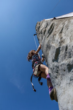 Young girl climbing on vertical wall with ropes outdoors warm summer day with clear blue sky.