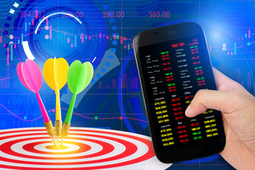 Hand holdind smartphone and stock charts screen with target center of dartboard with sunshine...