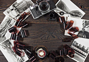 Old camera, film and black and white photographs are on the dark wooden surface