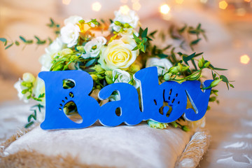 Wooden blue inscription Baby, on the background bouquet of white roses