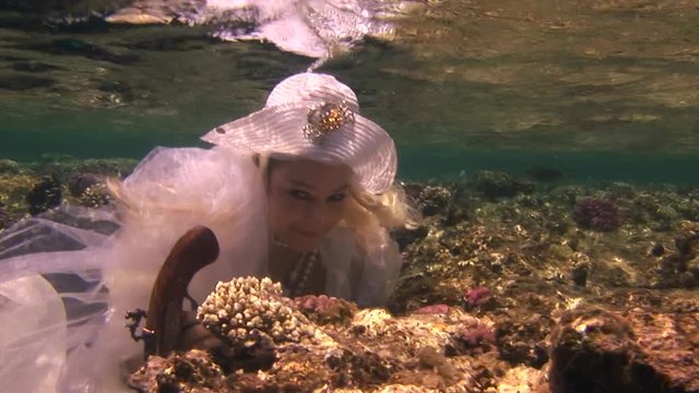 Model in white costume of pirate underwaterin Red Sea. Filming a movie. Young girl smiling at camera. Marine landscape, coral reefs, ocean inhabitants.