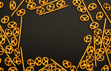 Background texture of salted salty pretzels and mini sticks in the traditional form of the hinge assembly on a black background. Space for text.