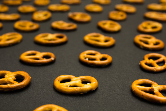 Background texture of salted savory mini pretzels in the traditional looped knot shape on the black background. Perspective.