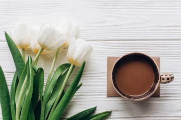 stylish tulips and morning coffee on white wooden rustic background. flat lay with flowers with space for text. hello spring concept. mothers or womens day morning