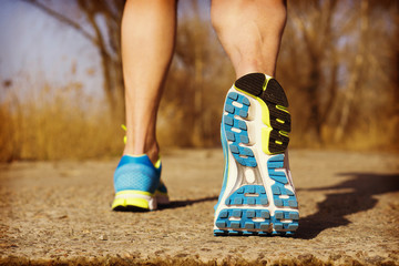 Back view of male muscular feet in sneakers walking on sidewalk in spring sunny day