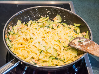 Frying zucchini, salmon and pasta in a pan