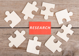 Jigsaw Puzzle Pieces with text "Research" on wooden background
