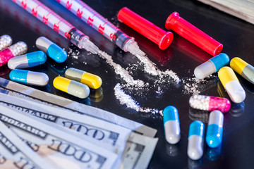 syringe with  heroine, pills, us money isolated on black glass.