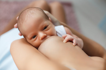 Happy young mother, sitting in the bedroom with her newborn son in her arms,gently supports the...
