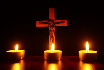 Crucifix and three burning candles in the darkness. Pray and hope.