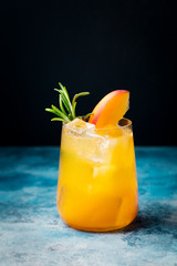 Peach cocktail, fizz with rosemary on blue stone background.