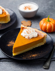 Pumpkin pie, tart made for Thanksgiving day on a black plate. Grey stone background.