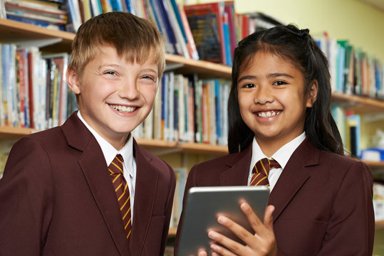 Portrait Of Pupils Wearing School Uniform Using Digital Tablet In Library