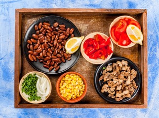 Ingredients for Mexican food on a tray: beans, stew beef, corn, tomatoes, red pepper, onion, herbs, tortillas taco, top view copy space