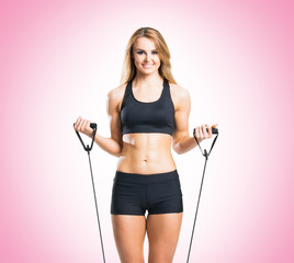 Fit, healthy and sporty woman in sportswear doing expander exercise pink background.