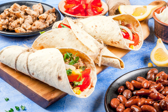 Street fast Mexican food, freshly prepared, homemade sandwiches burrito with beans, beef, corn, peppers, tomatoes and herbs. On the blue background of the concrete stone, copy space