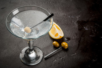 Cocktail martini with olives and a lemon on a black concrete stone table, copy space