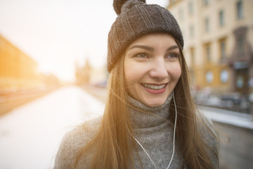 Beautiful girl with long hair in a sweater and a warm hat and smiling and listening to music on headphones white.
