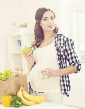 Beautiful pregnant woman with shopping bags in kitchen. Motherhood, pregnancy, maternity concept.