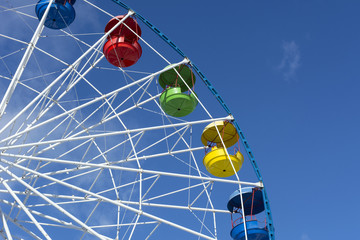 Ferris wheel with colored cabins on background of blue sky