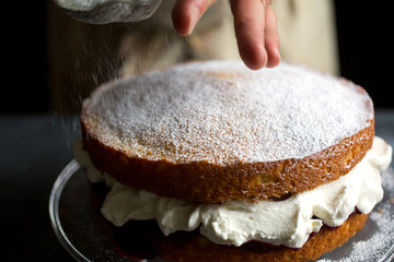 Person putting sugar on Victoria sponge cake, close-up