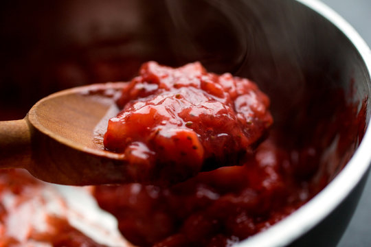 Strawberry reduction in saucepan and on wooden spoon, close-up