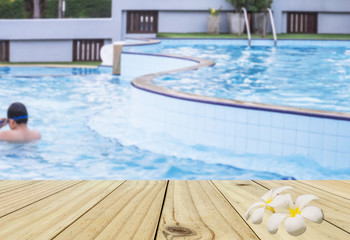 Blur of a boy in a swimming pool with white wood terrace and twin white plumeria flower
