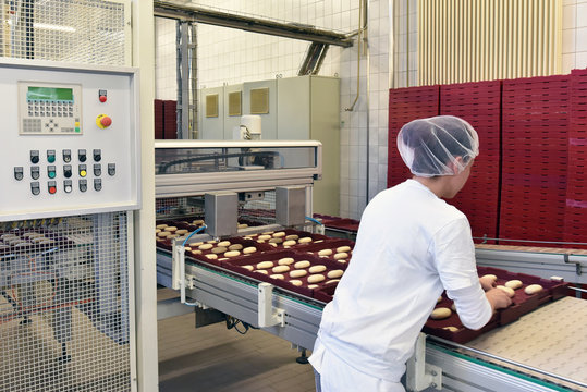 Frau arbeitet am Fliessband einer Gro&szlig;b&auml;ckerei // Woman is working on the conveyor belt of a bakery
