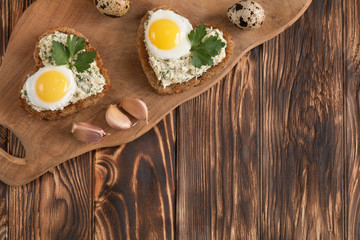 a sandwich in the shape of a heart with egg, cheese, dill, garlic on a wooden table
