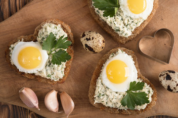 a sandwich in the shape of a heart with egg, cheese, dill, garlic on a wooden table