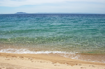 Yellow sand, footprint and an emerald sea water on the Greek beach.