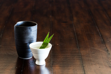 A black Sake jar and a white sake cup on the wood table.
