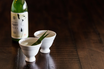 Two white sake cups and a bottle of sake on the rustic wood table.