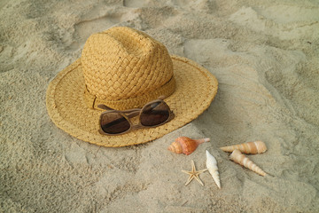 Natural color straw hat and brown sunglasses on the sandy beach with little seashells, Thailand 