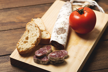 Fuet sliced bread and tomato on a wooden board. Spanish sausage. Horizontal shoot..