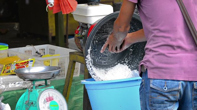 Worker grinds coconut meat from shell using gas powered machine at market