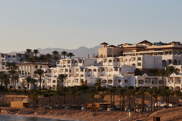 Obraz premium view of the white hotel and the beach. palm trees, summer sea and the mountains. Mural