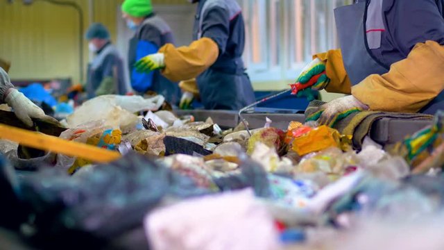 Workers at conveyor sorting garbage at a recycling plant. 4K.
